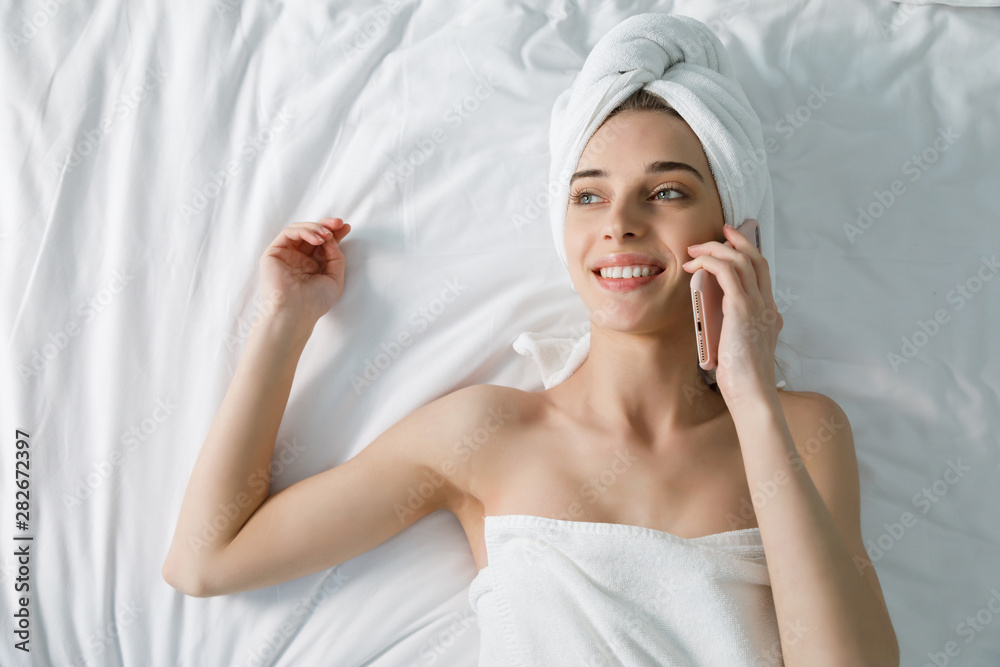 Young woman in white bath towel chatting on mobile phone in bed at home Young woman in white bath towel chatting on mobile phone in bed at home
