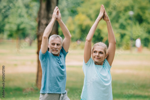 mature sportsman and sportswoman stretching with raised hands while training in park