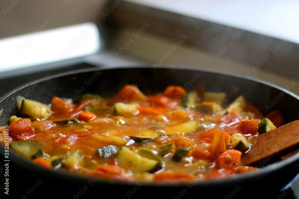 Cooking vegetables in a pan: zucchini, tomato and carrot. Selective focus.
