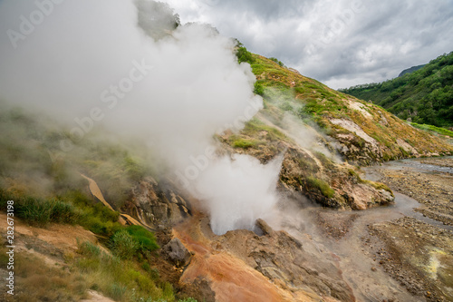 Geyser eruption in the Valley of Geysers in Kronotsky Nature Reserve, Kamchatka Peninsula, Russia. Colorful hill slope of Geysernaya River. Volcanic clay, and geothermal waters surrounding the scene. 