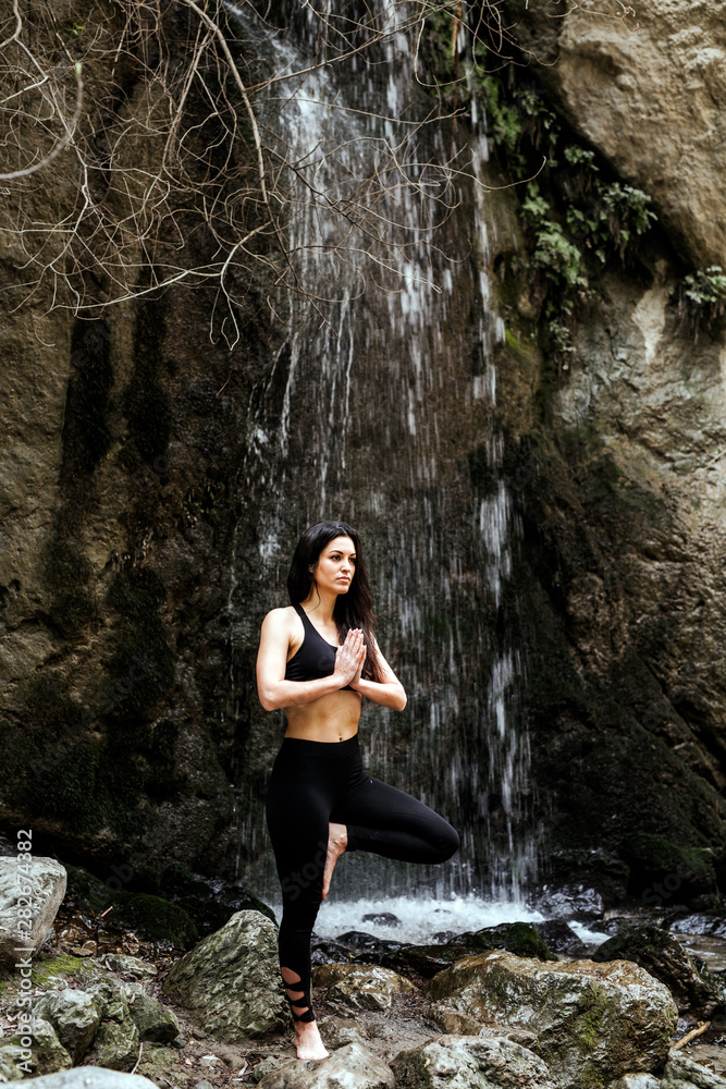Woman practicing yoga at waterfall, tree position Woman practicing yoga at waterfall, tree position