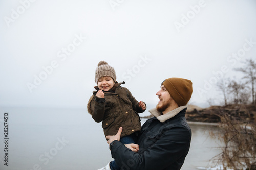 Happy family having fun on the cold river background. Dad puts her daughter up. photo