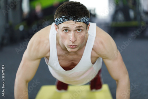 Front view portrait of caucasian guy making plank or push ups exercise, training indoors