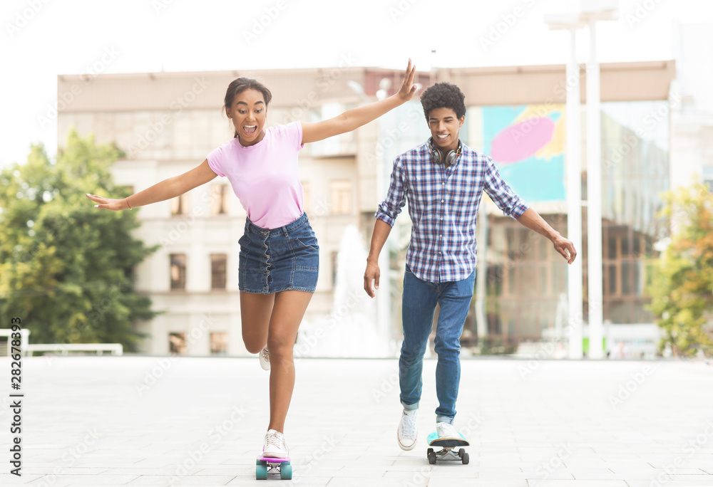 Happy teenage couple riding modern cruiser skateboards on city street