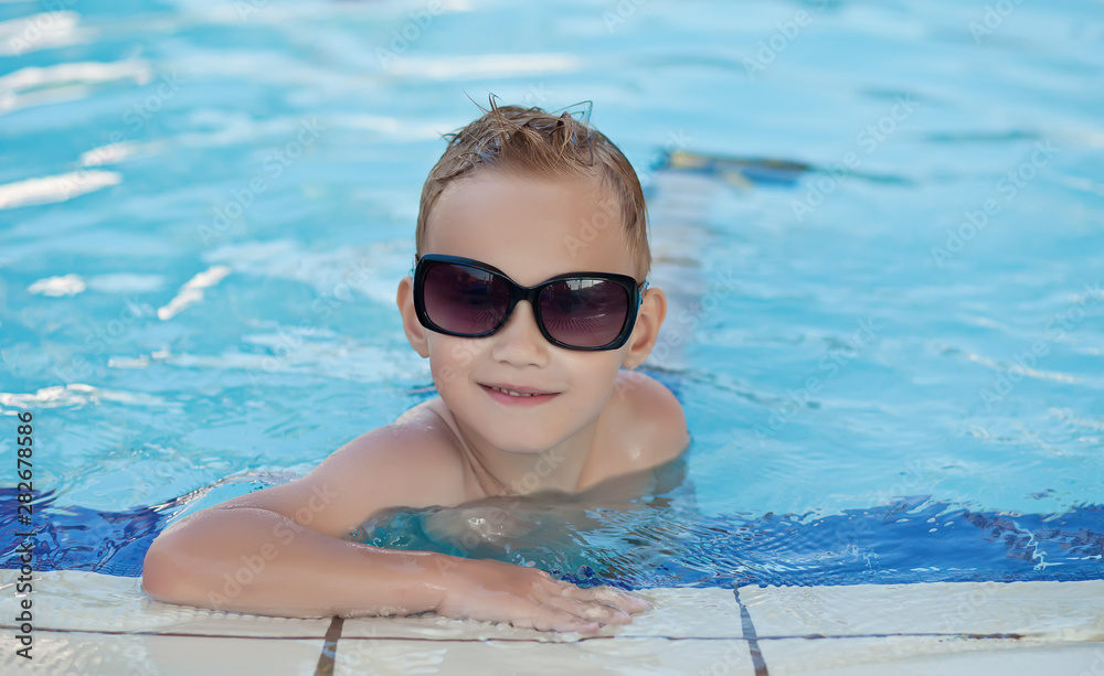 Happy boy with blond hair smiling sitting in swimming pool
