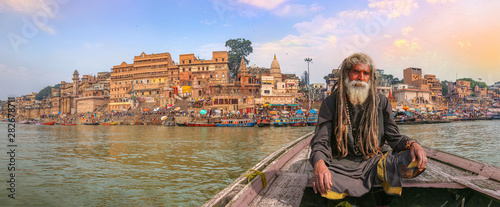 Indian sadhu on a wooden boat overlooking panoramic view of ancient Varanasi city architecture with Ganges river ghat photo