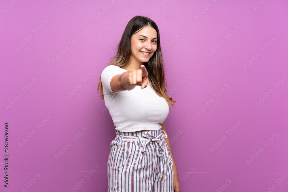 Young woman over isolated purple background points finger at you with a confident expression Young woman over isolated purple background points finger at you with a confident expression