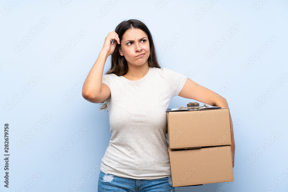 Young delivery woman over blue brick wall having doubts and with confuse face expression Young delivery woman over blue brick wall having doubts and with confuse face expression