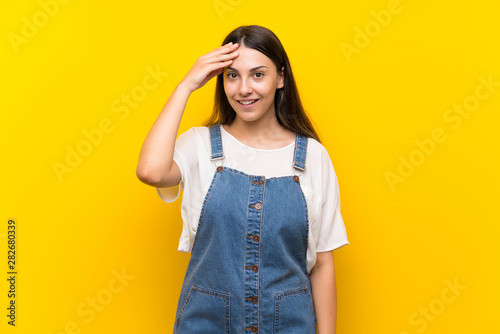 Young woman in dungarees over isolated yellow background has just realized something and has intending the solution