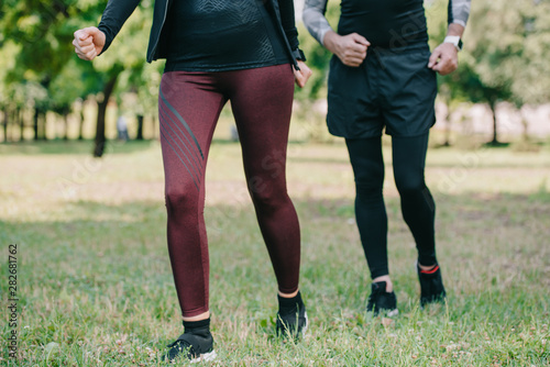cropped view of mature sportsman and sportswoman jogging in park