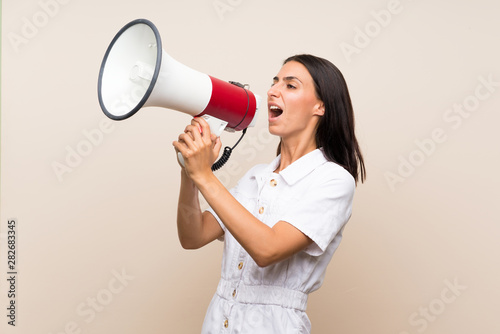 Young woman over isolated background shouting through a megaphone