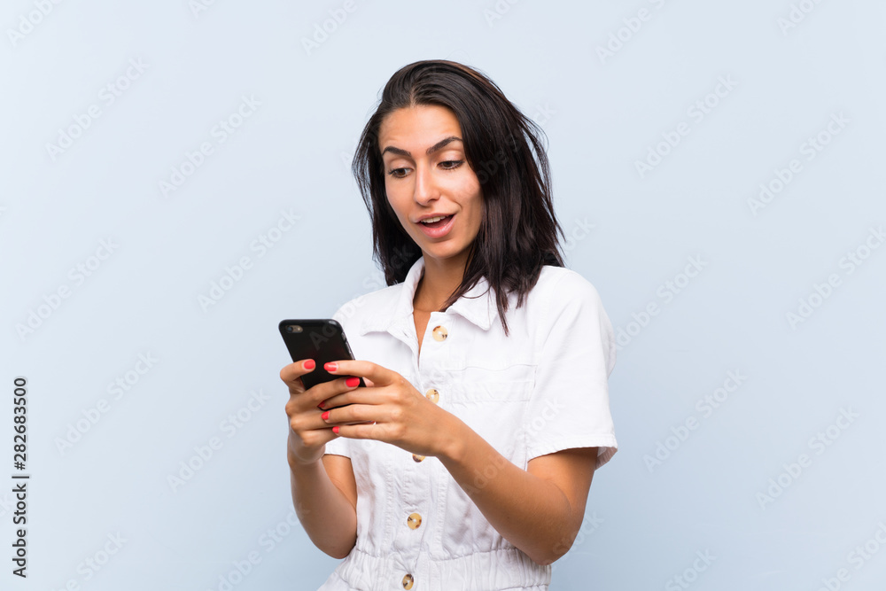 Young woman with a mobile phone over isolated blue wall Young woman with a mobile phone over isolated blue wall