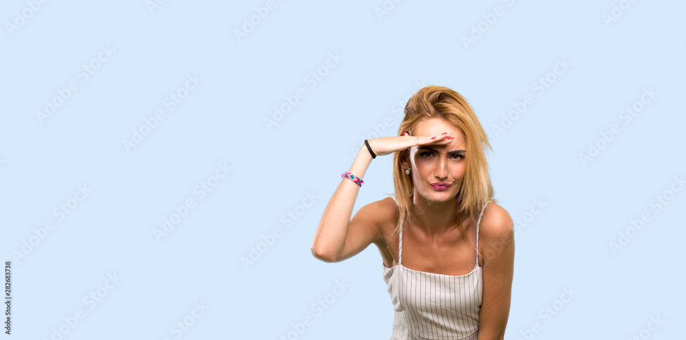 Young blonde woman looking far away with hand to look something over isolated blue background Young blonde woman looking far away with hand to look something over isolated blue background