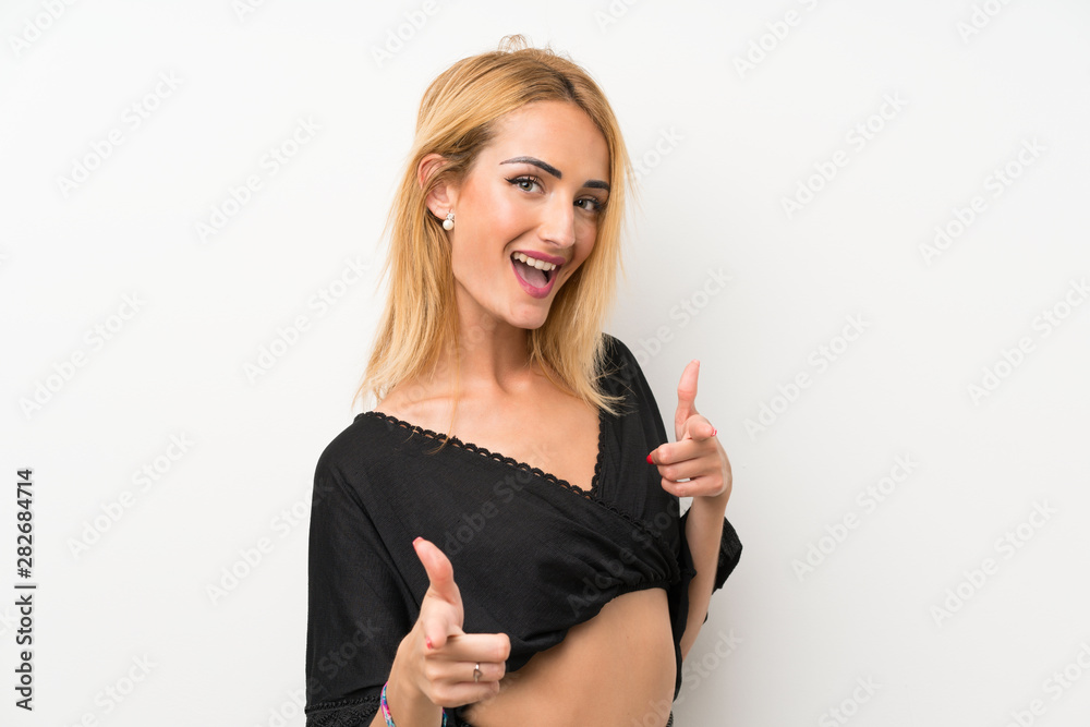 Young blonde woman over isolated white wall pointing to the front and smiling Young blonde woman over isolated white wall pointing to the front and smiling