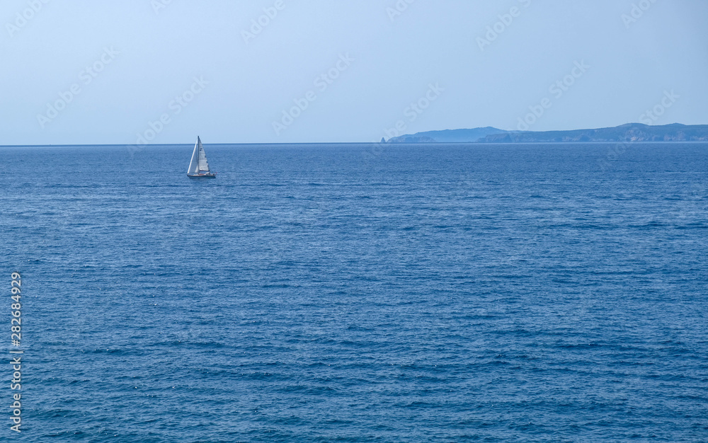 Single white boat sailing on calm water, along the coast of the Mediterranean on the background of the islands. Water activities, vacation at sea, happy holidays in the sea.