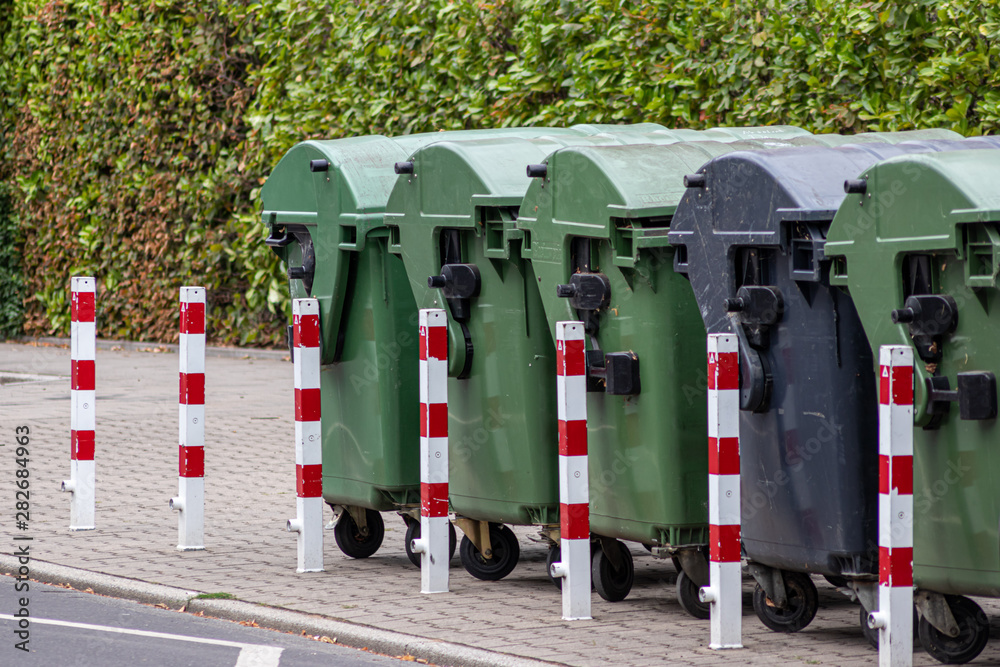 Große grüne Müllcontainer auf Rollen und schwarzer Rollcontainer für Müll und Abfälle stehen an