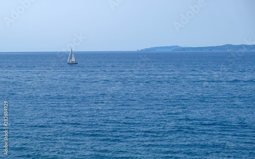 Single white boat sailing on calm water, along the coast of the Mediterranean on the background of the islands. Water activities, vacation at sea, happy holidays in the sea.