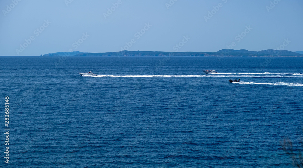 Motor boats sail on the sea on calm water in the sunny day, along the coast of the Mediterranean on the background of the islands. Water activities, summer time at sea, happy holidays in the sea.