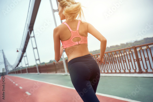 Sport is my life. Back view of young and slim woman in sports clothing jogging on the bridge