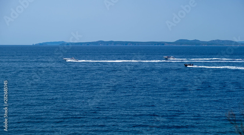 Motor boats sail on the sea on calm water in the sunny day, along the coast of the Mediterranean on the background of the islands. Water activities, summer time at sea, happy holidays in the sea. © Olga