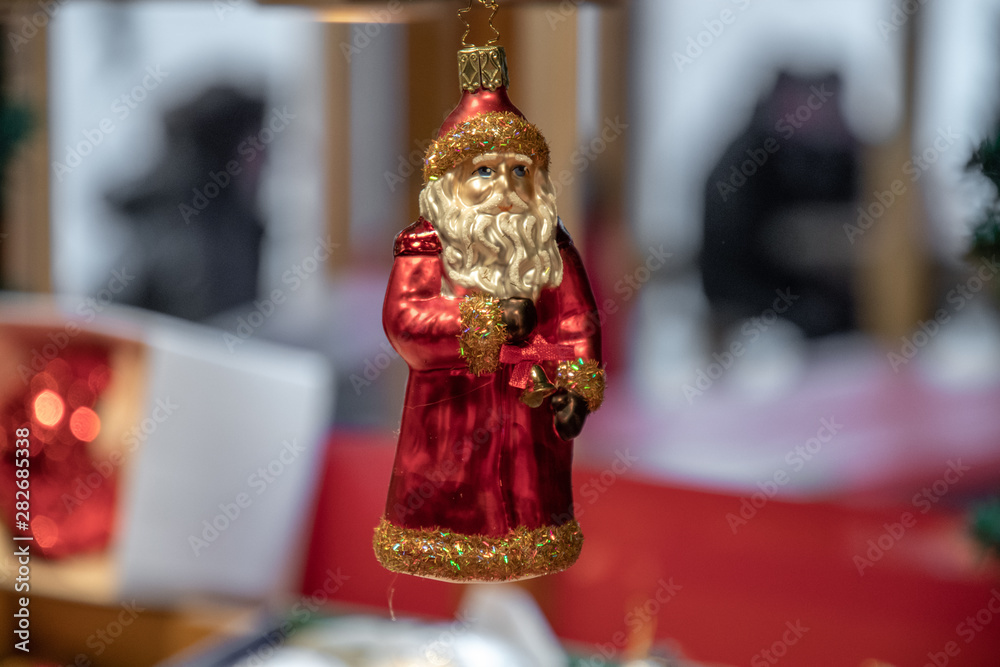 Retro style Santa Claus shaped Christmas ornament closeup on bokeh blurry background. Red and golden painted glass Christmas ornament is hanging against blurred window. New Year traditional decoration