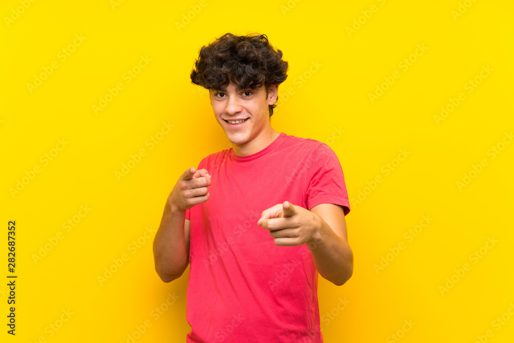 Young man over isolated yellow wall points finger at you Young man over isolated yellow wall points finger at you