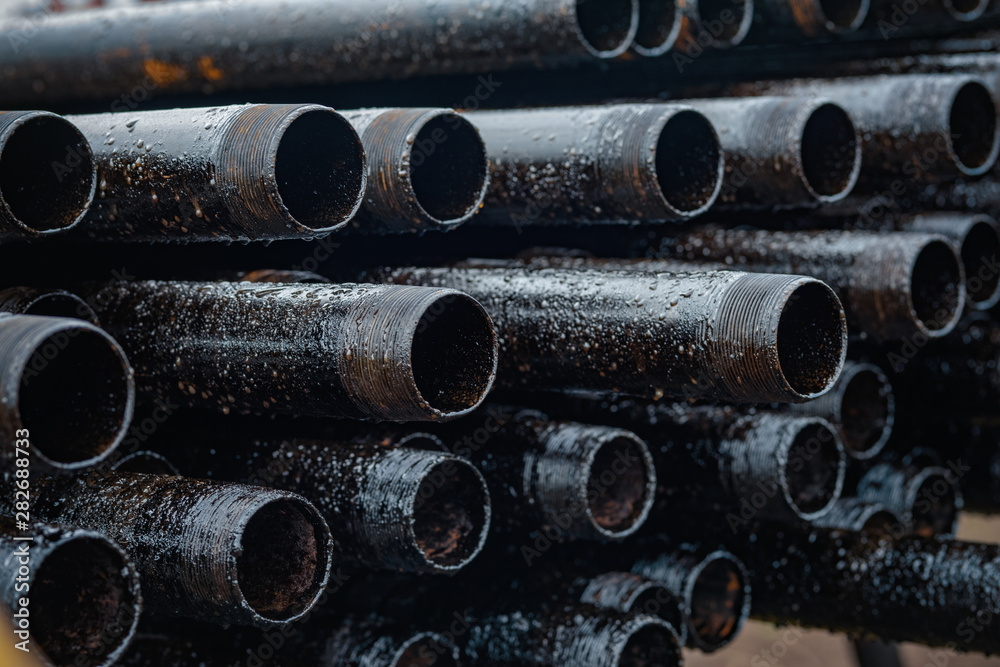 Oil Drill pipe. Rusty drill pipes were drilled in the well section. Downhole drilling rig. Laying the pipe on the deck. View of the shell of drill pipes laid in courtyard of the oil and gas warehouse Oil Drill pipe. Rusty drill pipes were drilled in the well section. Downhole drilling rig. Laying the pipe on the deck. View of the shell of drill pipes laid in courtyard of the oil and gas warehouse