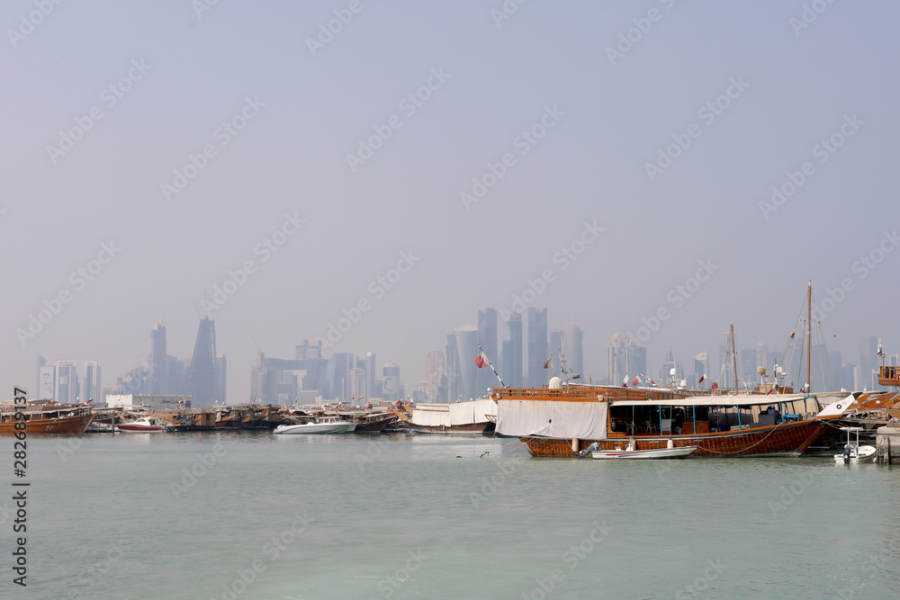Doha / Qatar – October 10, 2018: Traditional dhows moored up along the corniche in the Qatari capital Doha, with the skyscrapers of the West Bay area in the background