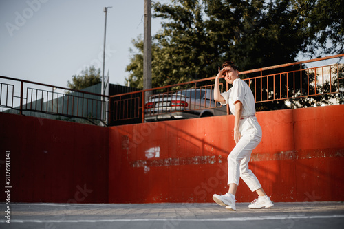 Young girl dressed in white shirt is dancing modern dance in the street on the background of parking in the sunny day