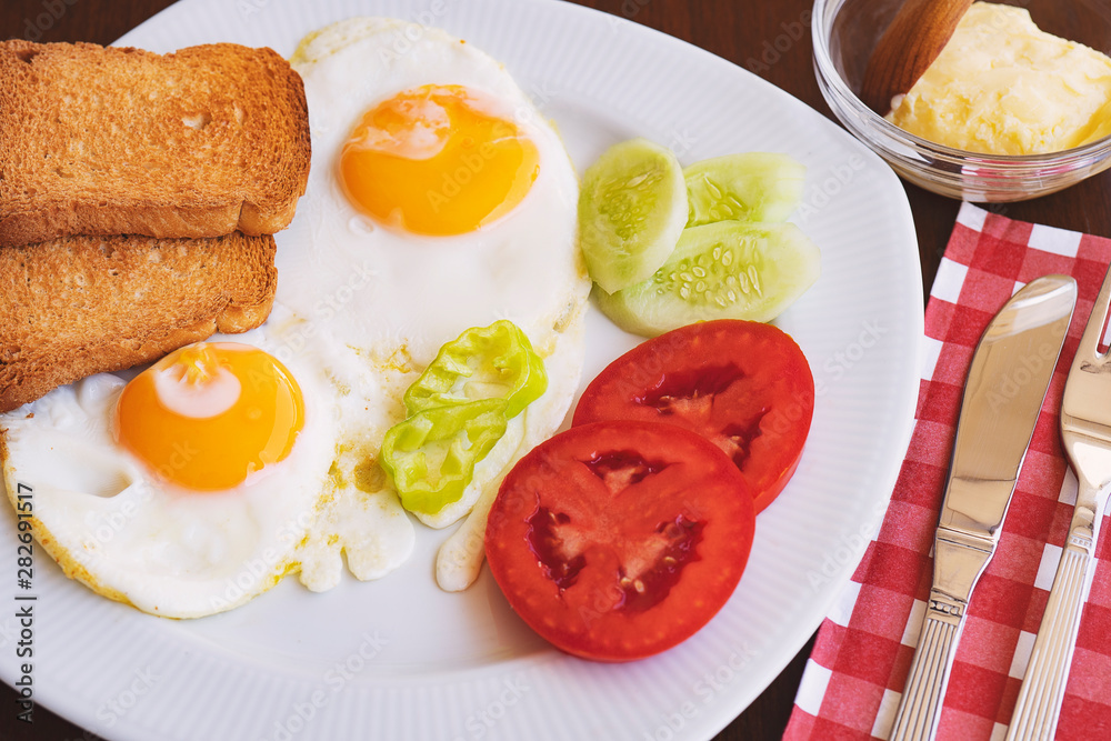Breakfast - fried eggs, butter and tomato in white plate. Close up image Breakfast - fried eggs, butter and tomato in white plate. Close up image
