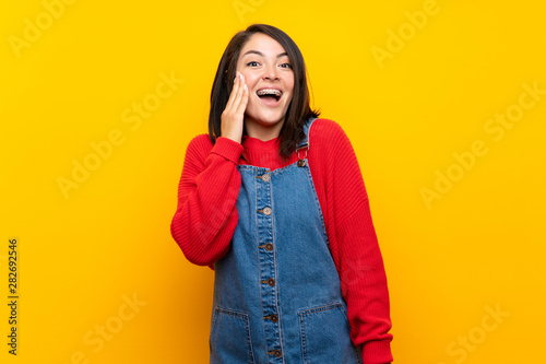 Young Mexican woman with overalls over yellow wall with surprise and shocked facial expression © luismolinero