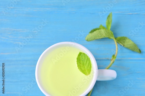 Curative mint tea in white porcelain cup with a green leaf of peppermint in tea and a sprig of fresh mint on blue textured wooden background. Healing hot mint tea. Calming peppermint beverage 