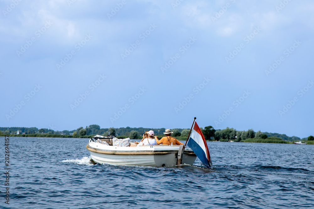 Tourists enjoying ride in white luxury motor boat with dutch flag. Summer vacation or boat rent theme.