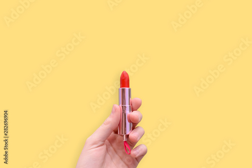 Red lipstick in a hand on a yellow background. Attributes of female cosmetics. Cosmetic product for applying makeup. Copy space