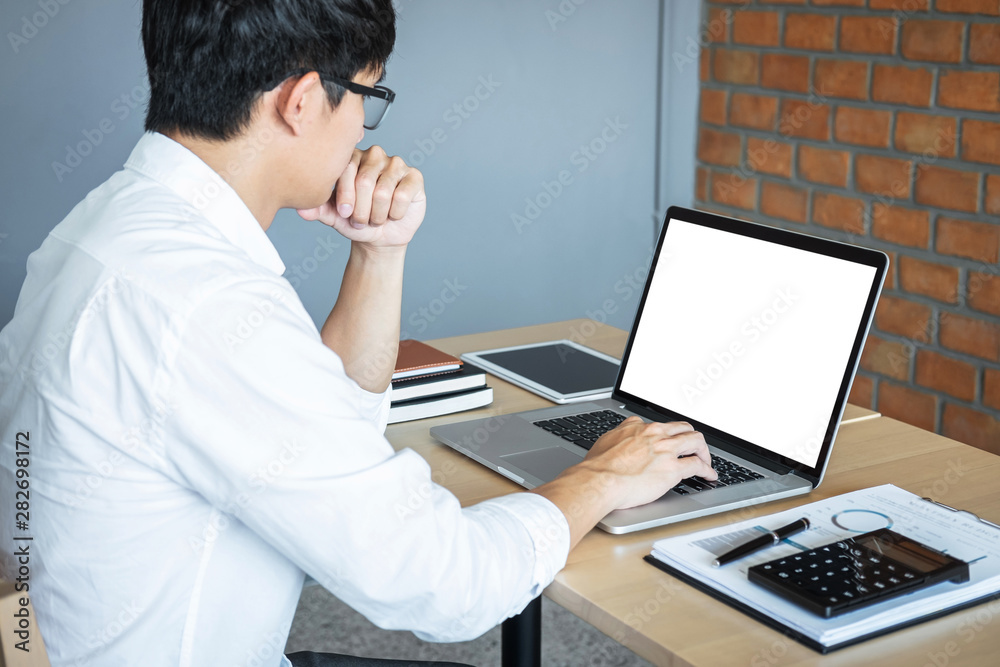 Image of Young man working in front of the laptop looking at screen with a clean white screen and blank space for text and hand typing information on keyboard in modern workspace Image of Young man working in front of the laptop looking at screen with a clean white screen and blank space for text and hand typing information on keyboard in modern workspace