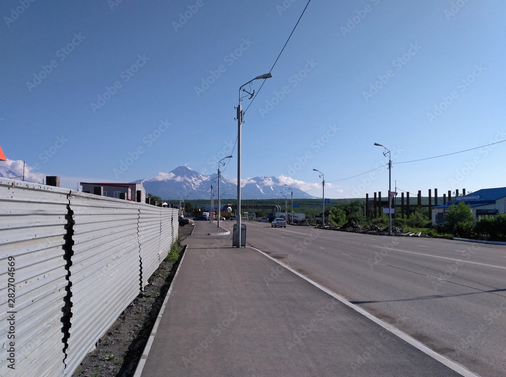 The empty modern street, the metal wall, lights and the far mountains on the summer sunny day.