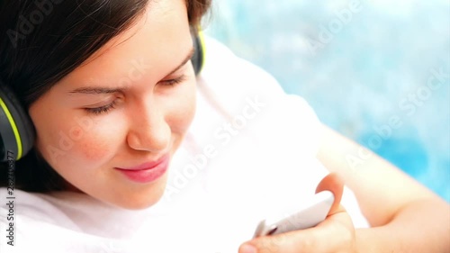 young girl in green headphones watch phone on a sunny day