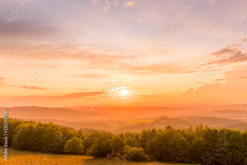 Sunset with view on landscape with fully colored clouds orange and purple and sun behind it and city Valasske Mezirici captured during summer late time. © Lukas