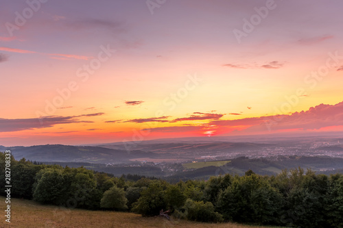 Sunset with view on landscape with fully colored clouds orange and purple and sun behind it and city Valasske Mezirici captured during summer late time.