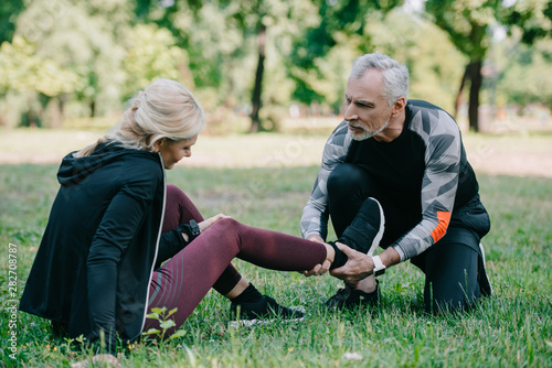 mature sportsman touching injured leg of sportswoman sitting on lawn in park © LIGHTFIELD STUDIOS