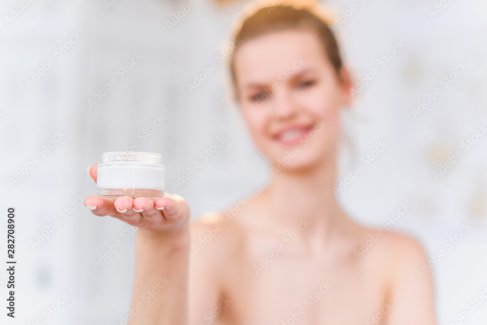 Attractive brunette woman opening jar with cream and smiling to the camera in the white stylish bathroom. Portrait shot. Attractive brunette woman opening jar with cream and smiling to the camera in the white stylish bathroom. Portrait shot.