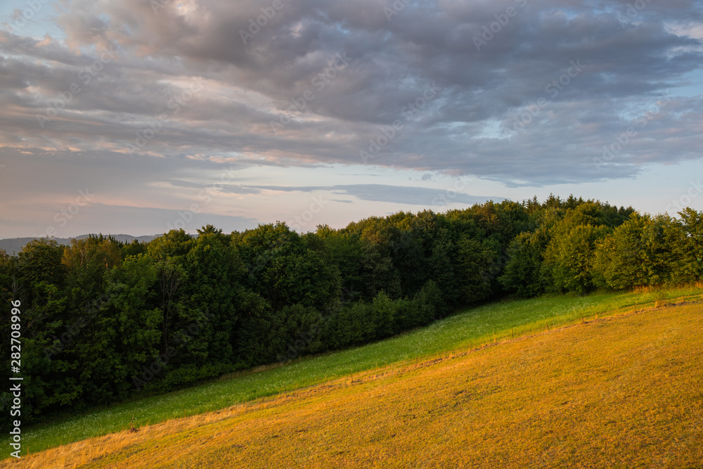 Obraz premium Meadow landscape countryside view with blue sky with many clouds sun light and forest close to city Valasske Mezirici captured during summer late time from hill.