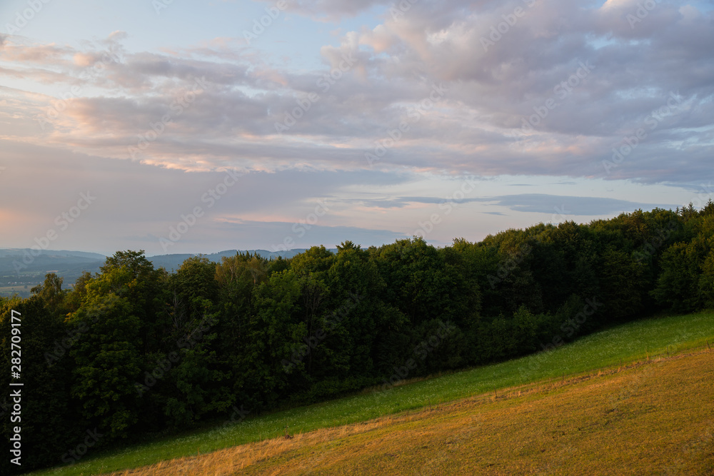 Obraz premium Meadow landscape countryside view with blue sky with many clouds sun light and forest close to city Valasske Mezirici captured during summer late time from hill.
