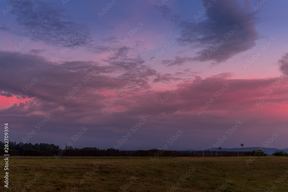 Landscape sunset with fully colored clouds pink orange sky look on meadow close to city Valasske Mezirici captured during summer late time.