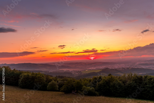 Sunset with view on landscape with fully colored clouds and orange sun goes down and city Valasske Mezirici captured during summer late time © Lukas