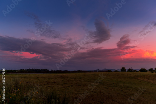 Landscape sunset with fully colored clouds pink orange sky look on meadow close to city Valasske Mezirici captured during summer late time. © Lukas