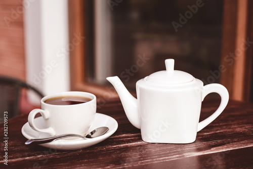 Teapot and a cup of tea on a wooden table in a summer cafe.