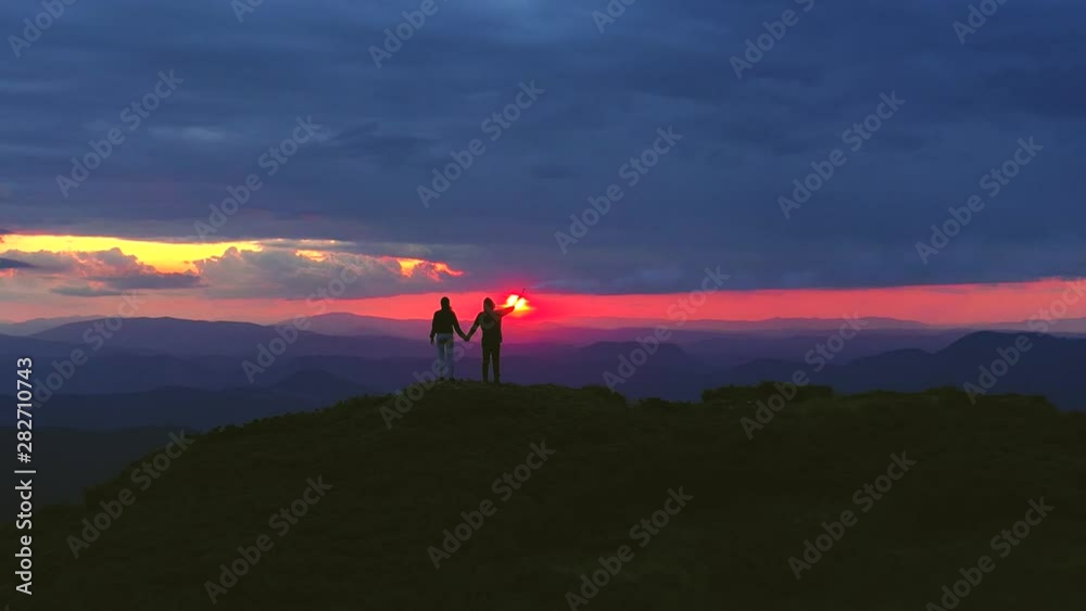 The couple with a firework stick standing on a mountain on a sunset background The couple with a firework stick standing on a mountain on a sunset background
