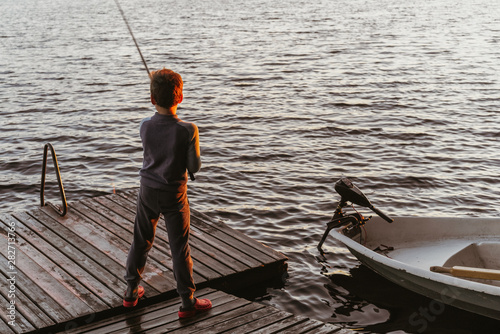 A young boy is fishing on a wooden pier at sunset