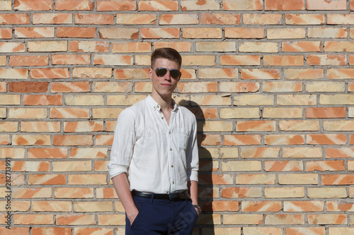 Smiling young man portrait with retro shiny drop sunglasses against brick wall